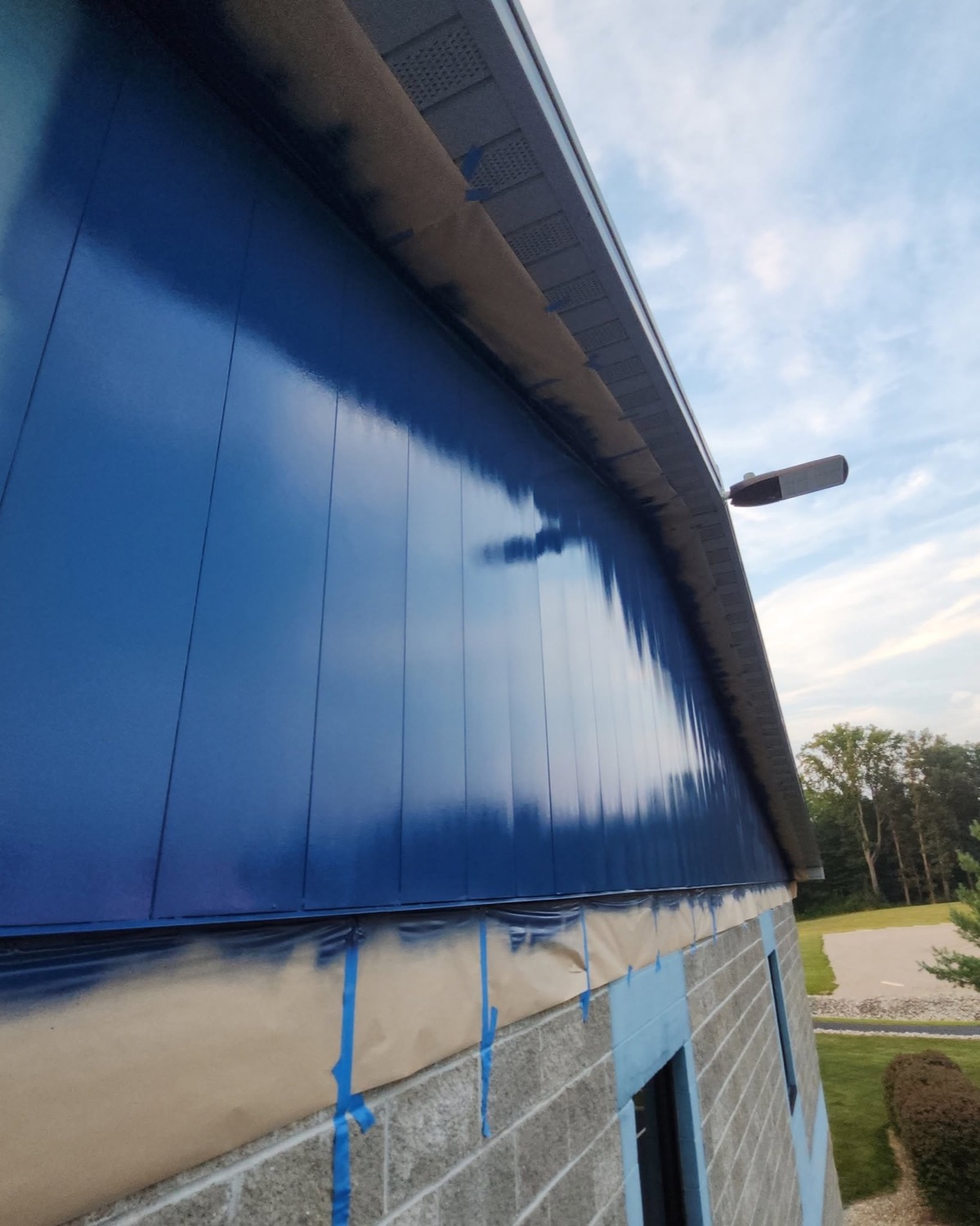 Commercial building's metal siding freshly sprayed in deep blue, with blue tape and paper masking the block wall below