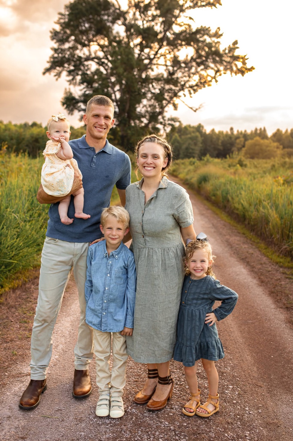 The Ikerd family: Ben holding their baby daughter, his wife, and their young son and daughter, standing on a gravel lane at sunset